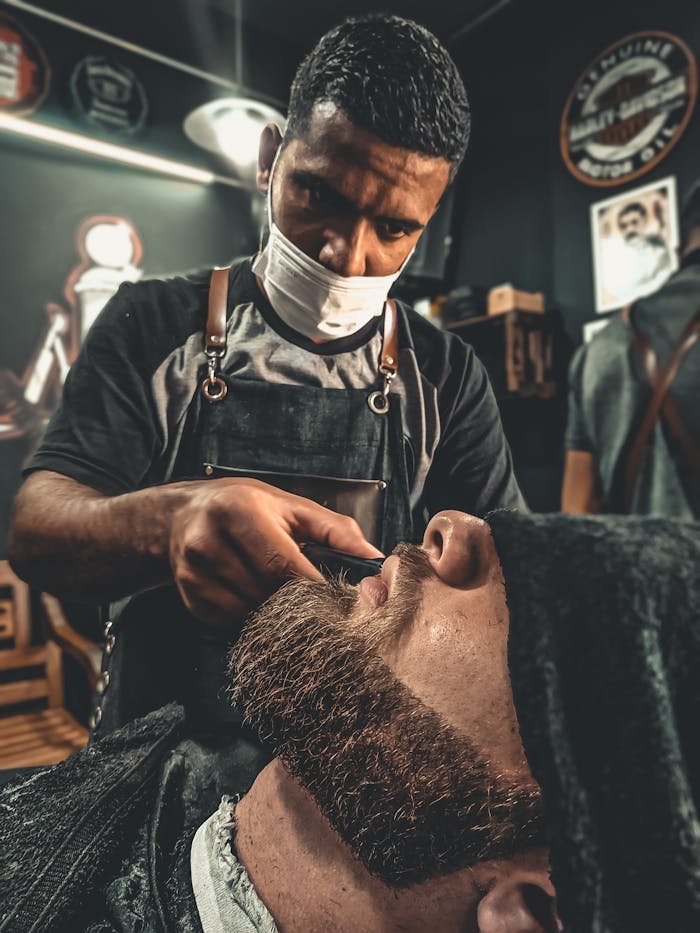 A barber meticulously trims a clients beard in a modern barbershop setting.