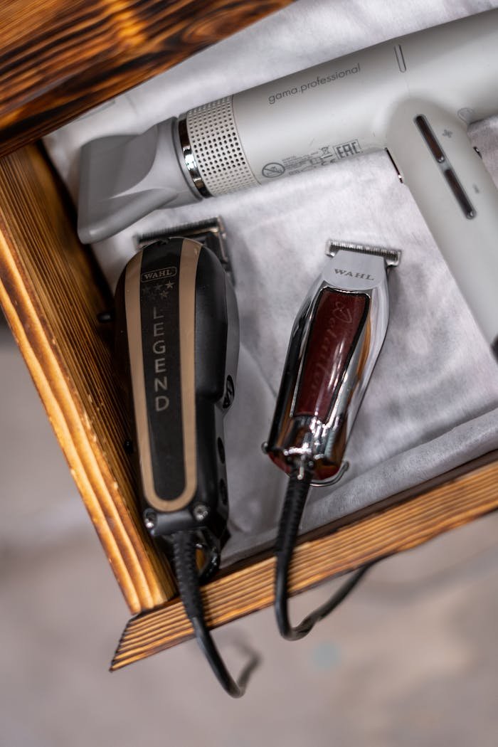 Close-up view of barber tools in a wooden drawer, including clippers and a hairdryer.